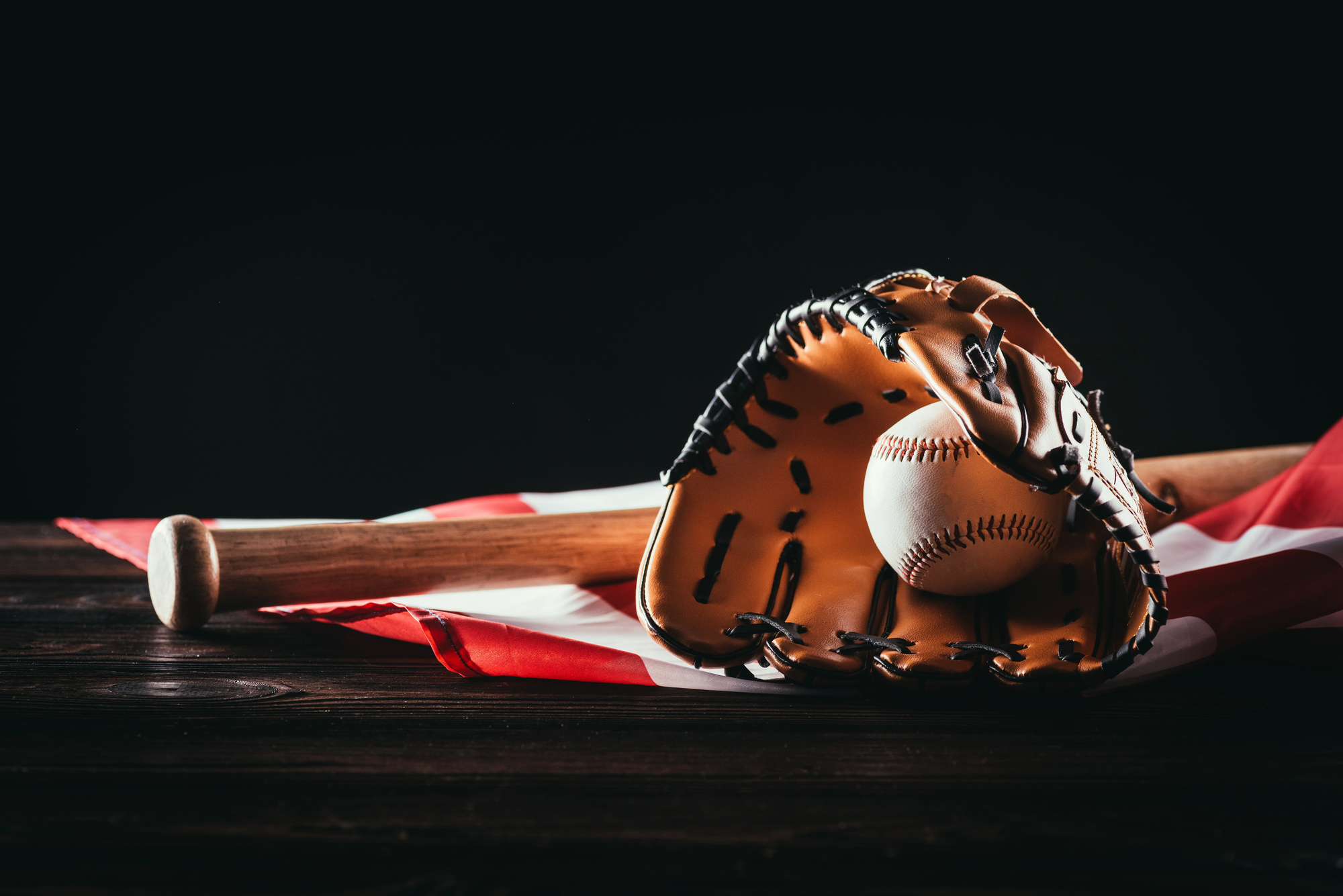 Close-up view of baseball glove with ball and bat on wooden table and us flag on black — Photo